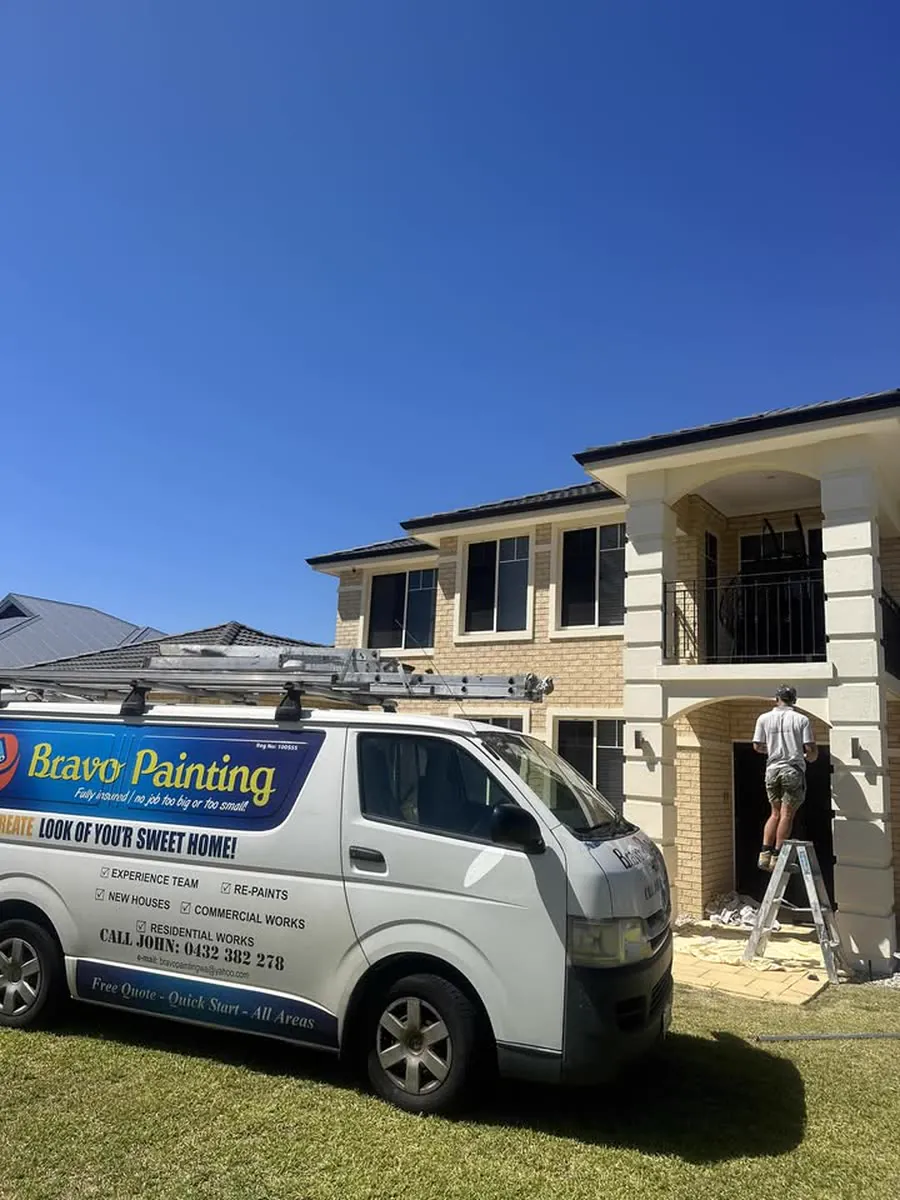 Bravo Painting's van outside a two-storey Perth home with a painter working at height